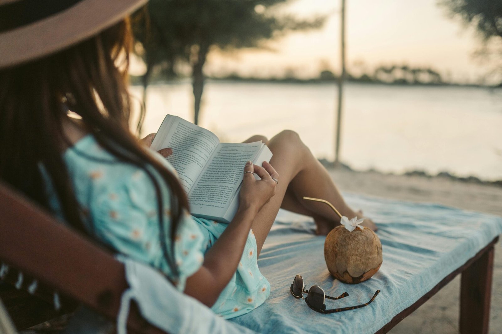 Woman in dress reading book by water